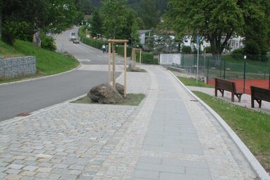 Das Bild zeigt die neu gestaltete Straße vom Tennisplatz zum Silberberg Hallen- und Freibad. Am Gehwegrand stehen Bäume und Bänke.  | © Markt Bodenmais