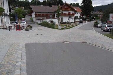 Blick in Richtung Finkenweg auf eine Kreuzung. Auch hier ist der Straßenbelag aus Teer und Granitpflaster erneuert worden. Im Hintergrund sieht man eine Häusersiedlung vor Bäumen.  | © Markt Bodenmais