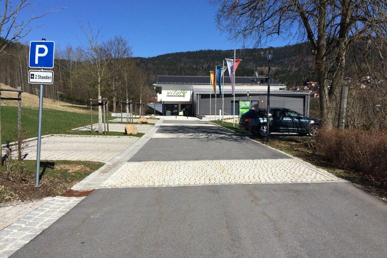 Im Vordergrund sieht man auch hier die neu geteerte Straße und die gepflasterten Parkbuchten. Im Hintergrund ein Haus in dem Sportkurse stattfinden.  | © Markt Bodenmais