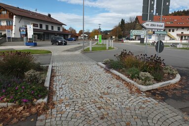 Die Fußgängerüberquerung mit Wegweisern ist hier im Vordergrund. Dahinter sieht man Geschäfte und einen Parkplatz.  | © Markt Bodenmais