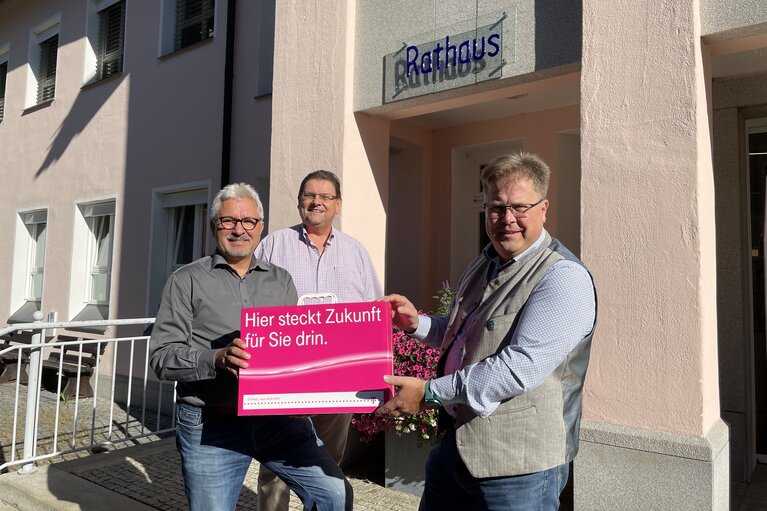 Drei Männer stehen vor dem Rathaus und präsentieren gemeinsam ein pinkes Schild. Auf dem Schild steht "Hier steckt Zukunft für Sie drin." | © Markt Bodenmais